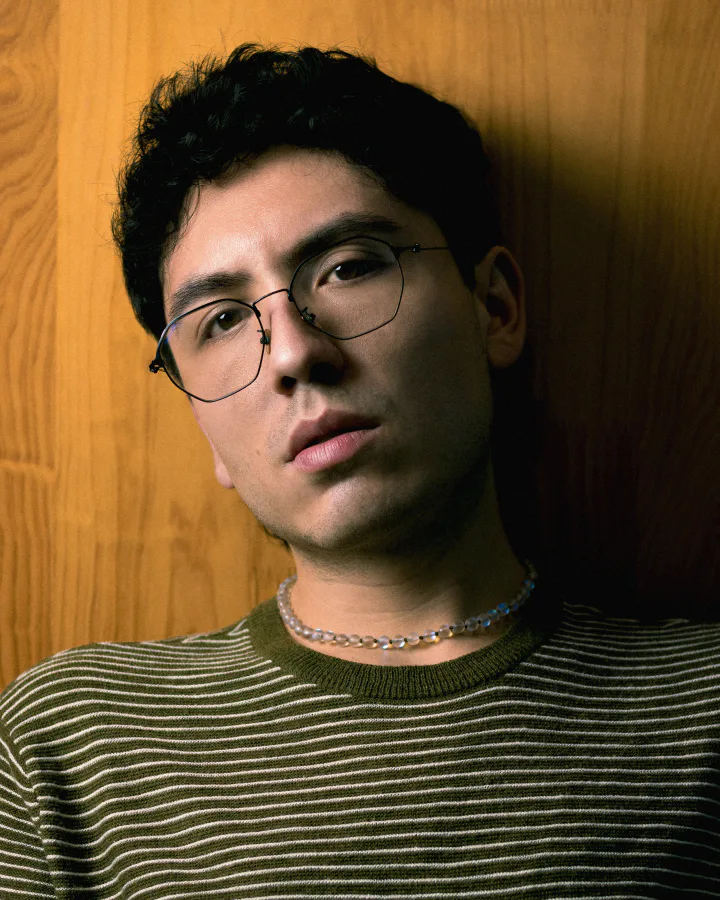 Retrato editorial de BLUEMAD con gafas frente a una pared de madera
